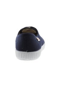 Scarpa slip-on in tela blu navy con retro arrotondato, suola in gomma bianca e motivo del battistrada testurizzato. Etichetta del marchio rossa e bianca visibile di lato.