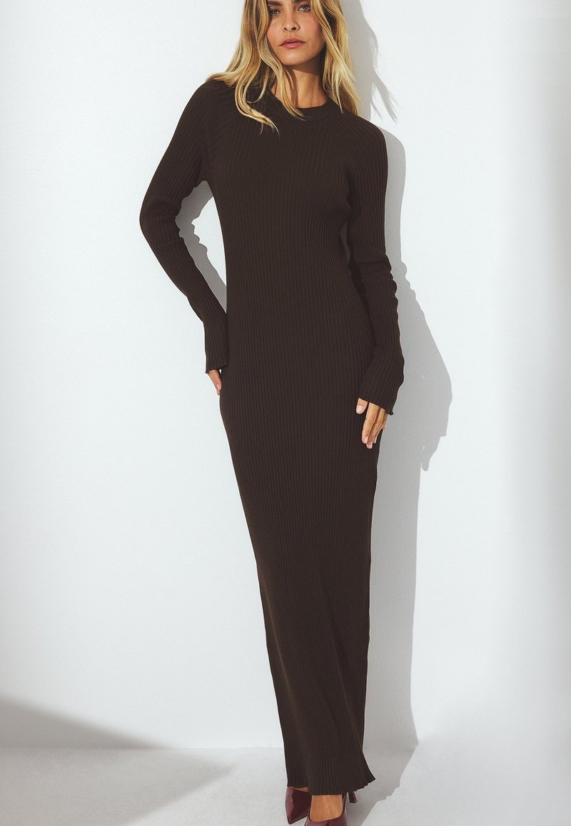 Pikk, ribaga sviiterkleit tumepruunis, millel on pikad varrukad ja ümmargune kaelus, sirge siluett ning külgmine lõhik allääres.