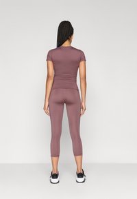 Fitnesa ap�ģērba komplekts mauve krāsā, sastāv no īsām piedurknēm un capri biksēm, ar gludu, elastīgu materiālu un bez redzamām logo.