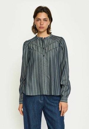 Striped blouse in dark blue with light vertical stripes, buttoned front, collar, and gathered shoulder details. Paired with denim pants.