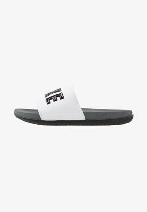 Nike sandále s bielym syntetickým pásikom, ktorý má vyvýšené čierne logo. Tmavošedá polstrovaná podrážka s textúrovaným vzorom pre lepšiu priľnavosť.
