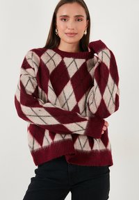 Zachte, oversized trui met een bordeauxrood en crèmekleurig ruitpatroon, vergezeld van grijze accenten en een geribbelde halslijn, mouwen en onderste zoom.