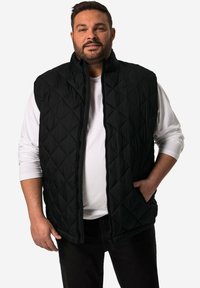 Schwarze gesteppte Weste mit hohem Kragen, mit einem Frontreißverschluss und zwei Taschen, getragen über einem weißen Langarmshirt.
