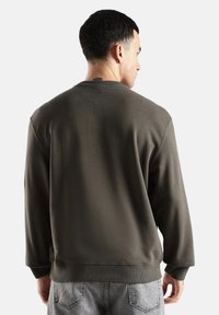 Sudadera verde oliva oscuro con cuello redondo, puños y dobladillo acanalados. Hecha de material suave, presenta un diseño simple y limpio.