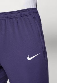 Lila Sporthosen aus weichem Stoff verfügen über einen elastischen Bund und ein weißes Nike-Logo auf der linken Seite.