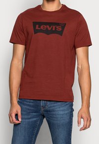 Rød bomulds t-shirt med et stort sort Levi's-logo design på forsiden. Rund hals og korte ærmer, parret med blå jeans.