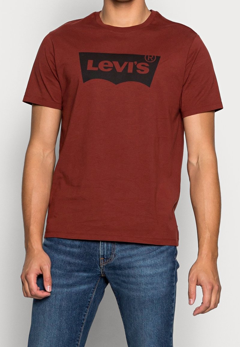 Rød bomulds t-shirt med et stort sort Levi's-logo design på forsiden. Rund hals og korte ærmer, parret med blå jeans.