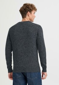 Mørkegrå strikkegenser med rund hals, lange ermer og ribbestrikkede mansjetter. Har et strukturert mønster og en avslappet passform.