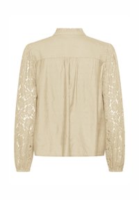 Blouse beige à manches longues, avec des panneaux latéraux en dentelle, un dos froncé et un col montant. Fabriquée en tissu léger texturé.
