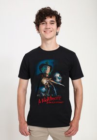 Schwarzes T-Shirt mit einem Grafikdesign zu "A Nightmare on Elm Street". Das Design zeigt eine bedrohliche Gestalt mit Klauen und ein verzweifeltes Gesicht im Hintergrund.