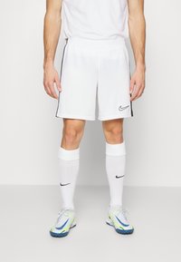 Vita sportiga shorts med svarta sidostripes och Nike-logga. Kombinerat med vita knästrumpor och flerfärgade sportskor med blå accent.