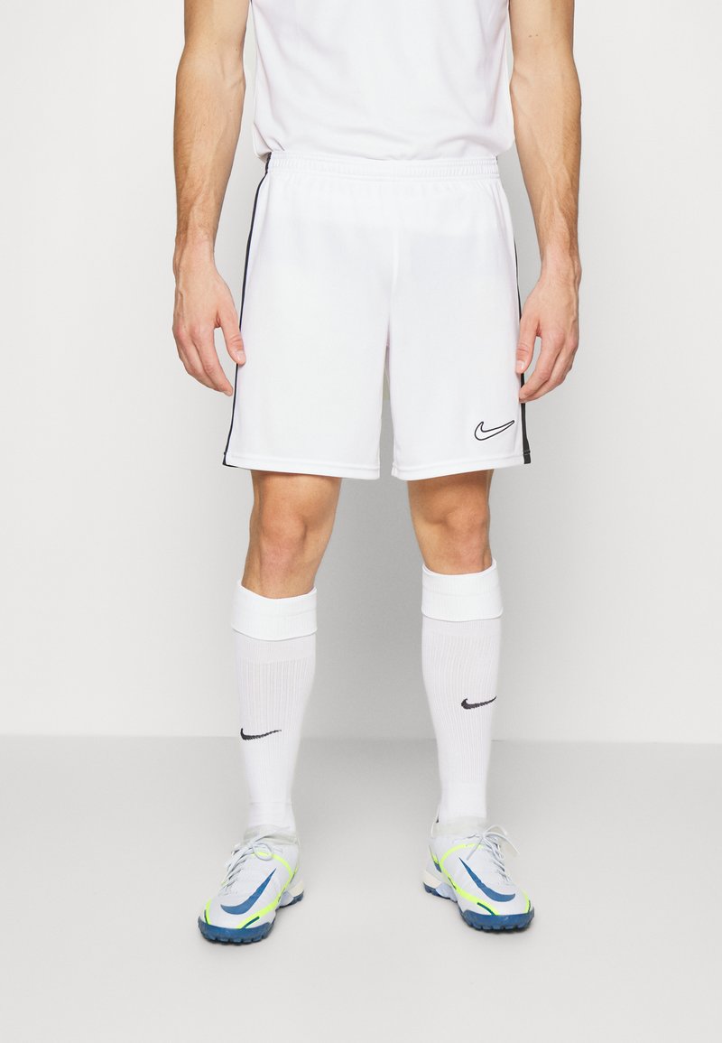Vita sportiga shorts med svarta sidostripes och Nike-logga. Kombinerat med vita knästrumpor och flerfärgade sportskor med blå accent.