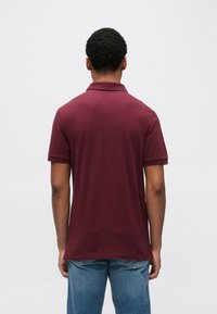 Bordowa koszulka polo z kołnierzykiem, krótkimi rękawami i prostym dołem. Wykonana z gładkiej tkaniny, z fakturowanym wykończeniem na kołnierzyku.