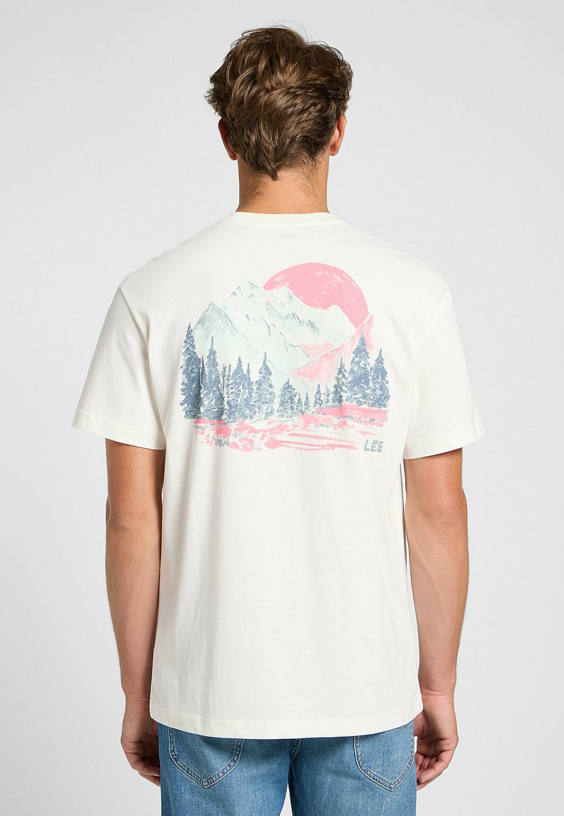 Camiseta de manga corta color crema con un gráfico colorido de montañas y bosques en la parte trasera, con un gran sol rosa y el nombre de la marca "LEE".