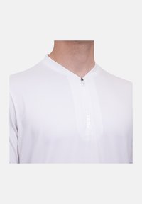 Maglietta bianca a maniche corte con zip a metà. Presenta un colletto e un tessuto liscio e leggero con una lieve trame. Senza motivi o dettagli.