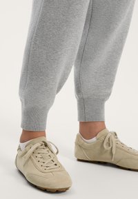 Beige suede athletic shoes with laces, paired with light grey tapered sweatpants featuring ribbed cuffs. Smooth texture, casual design.