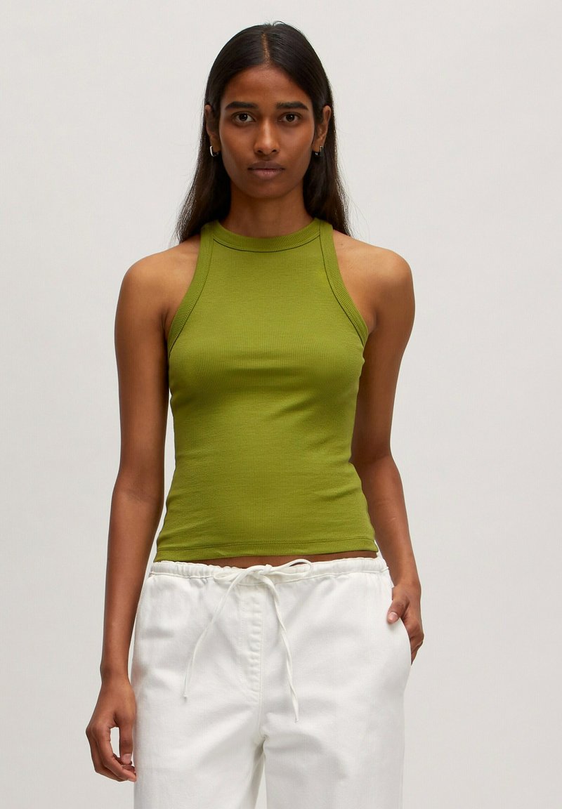 Geribbelde groene tanktop met hoge hals en mouwloos ontwerp, gecombineerd met witte broek met trekkoord. Gladde textuur, aansluitende pasvorm.