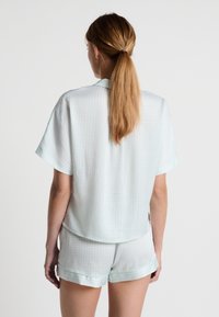 Maglietta da pigiama a maniche corte di colore verde menta con un motivo geometrico, abbinata a pantaloni corti. Entrambi realizzati in tessuto morbido con una vestibilità comoda e orli arrotolati.