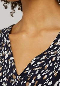 Robe bleu marine avec un décolleté en V, présentant un motif à petits pois en blanc et tons marron. Tissu doux avec une texture lisse.