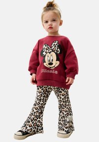 Roter Sweatshirt mit einem Minnie Mouse Grafik und einer leopardgemusterten Schleife. Ausgestellte Hose mit Leopardenmuster, die eine Textur und ein Markenschild hat. Schwarze Sneaker.
