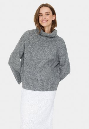 Chunky gray knit sweater with a cowl neckline, wide sleeves, and a relaxed fit, paired with a white textured skirt. Soft, warm material.