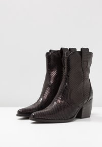 Bottes de cowboy noires avec un motif de serpent texturé, bout pointu et petit talon empilé. Équipées de brides pour un enfilage facile.
