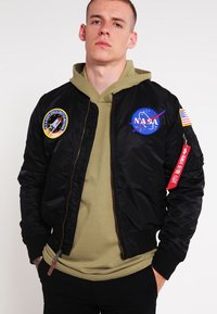 Černá nylonová bomber bunda s nášivkami NASA a vesmírných misí, zapínání na zip, žebrované manžety a červený štítek na levém rukávu.