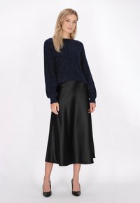 Navy gestrickter Pullover mit Schimmer, Rundhalsausschnitt und Ballonärmeln; schwarzer Satin-Midi-Rock mit glatter Textur und fließendem Schnitt.