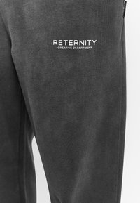 Dark grey sweatpants made of soft fabric, featuring white logo text "RETERNITY CREATIVE DEPARTMENT" on the left side, with a straight cut.