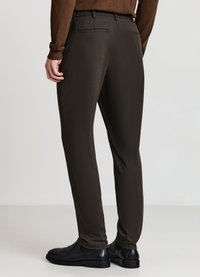 Dunkelbraune, elastische Bundhose mit glatter Textur, schlanker Passform und zwei Gesäßtaschen, kombiniert mit schwarzen Schuhen.