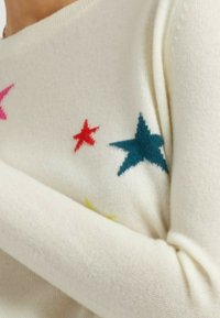 Maglione crema con motivi di stelle colorate in rosa, rosso, teal e giallo. Tessuto morbido, scollatura rotonda e maniche aderenti.