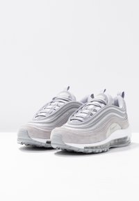 Ljusgrå atletiska sneakers med lager av mocka och syntetiska material, rund tå och en synlig luftkuddenhet i sulan.