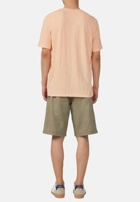 Jasnoróżowa koszulka z krótkim rękawem, wykonana z miękkiego materiału, w połączeniu z oliwkowymi szortami i beżowymi trampkami z niebieskimi akcentami.