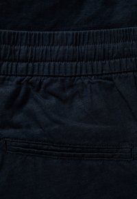 Tissu bleu marine foncé présentant une ceinture élastique et une poche arrière horizontale avec une ouverture cousue.