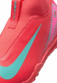 Kirkkaan vaaleanpunainen urheilukenkä, jossa on teksturoitu päällinen, ja siinä on näkyvä turkoosi swoosh sekä vedonauha. Joustava kumipohja, jossa on pito kuvio.