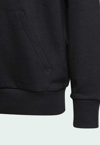 Felpa nera con tasca a marsupio, polsini e fondo a costine. Caratterizzata da una texture morbida e un design semplice, focalizzata sulla funzionalità e sul comfort.