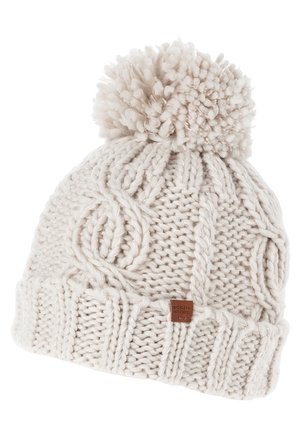 Bonnet d'hiver épais couleur crème avec un gros pompon sur le dessus et une petite étiquette de marque en cuir marron sur le revers.