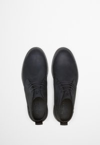 Chaussures en cuir noir avec une texture lisse, bout rond, couture subtile et design à lacets. Présente une languette au talon pour un enfilage facile.