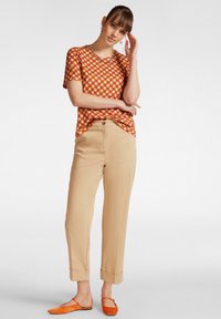 Blusa corta a maniche corte rossa e arancione con motivo a fantasia, abbinata a pantaloni beige a sigaretta e ballerine arancioni con punta affusolata.