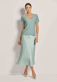 Lichtblauwe trui met korte mouwen en een ronde hals, gecombineerd met een zwierige mintgroene satijnen rok. Zilveren hoge hakken accentueren de outfit.