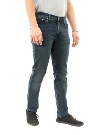 Dark blue denim jeans with a slim fit, featuring a zipper fly, five pockets, and subtle stitching details. Worn with black sneakers.