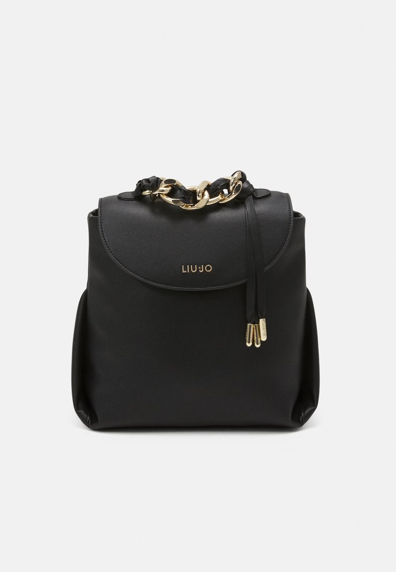 Sac à dos en simili cuir noir avec quincaillerie dorée, présentant un rabat arrondi, des accents en chaîne et deux franges latérales pour la fermeture.