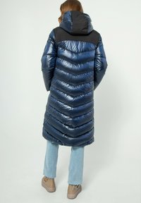 Giacca piumino blu navy con motivo a zigzag, finitura lucida e spalle nere. Presenta un cappuccio e un design di lunghezza media.