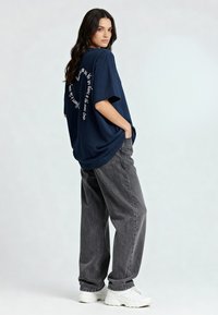 Tamsiai mėlynas per didelis marškinėliai trumpomis rankovėmis, ant nugaros yra baltas tekstinis dizainas. Derinami su pilkais plačiais džinsais ir baltais sportbačiais.