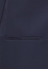 Tessuto blu navy che mostra una texture liscia, con una tasca piatta caratterizzata da un sottile dettaglio di cucitura. Design su misura con linee pulite.