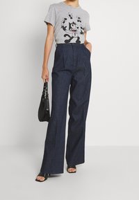 Grå t-shirt med en tecknad kattgrafik, kombinerad med högmidjade, mörk denimbyxor med vida ben. Accessoarer med en liten svart väska.