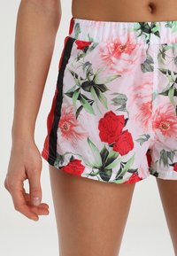 Ruusuilla ja vihreillä lehdillä varustetut vaaleanpunaiset kukkakuosiset uimaportit. Musta sivuraita ja joustava vyötärö. Kevyt kangas.