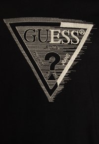 Schwarzes Baumwoll-T-Shirt mit einem großen, weißen gestickten Dreieck-Logo, auf dem "GUESS," "U.S.A" und ein Fragezeichen zu sehen sind, mit strukturierten Details.