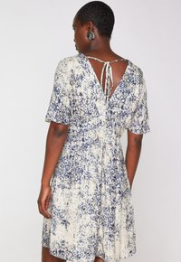 Abito a maniche corte color crema con stampa floreale blu, dotato di scollatura a V e dettaglio con laccio sul retro. Texture morbida e vestibilità comoda.