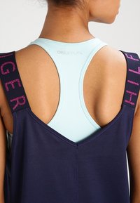 Navy sports tank top with wide straps, featuring textured pink lettering. Layered over a light blue fitted tank with a rounded neckline.